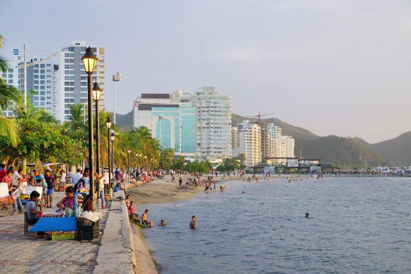 Foto de edificios y personas que van por un andén al lado de una playa